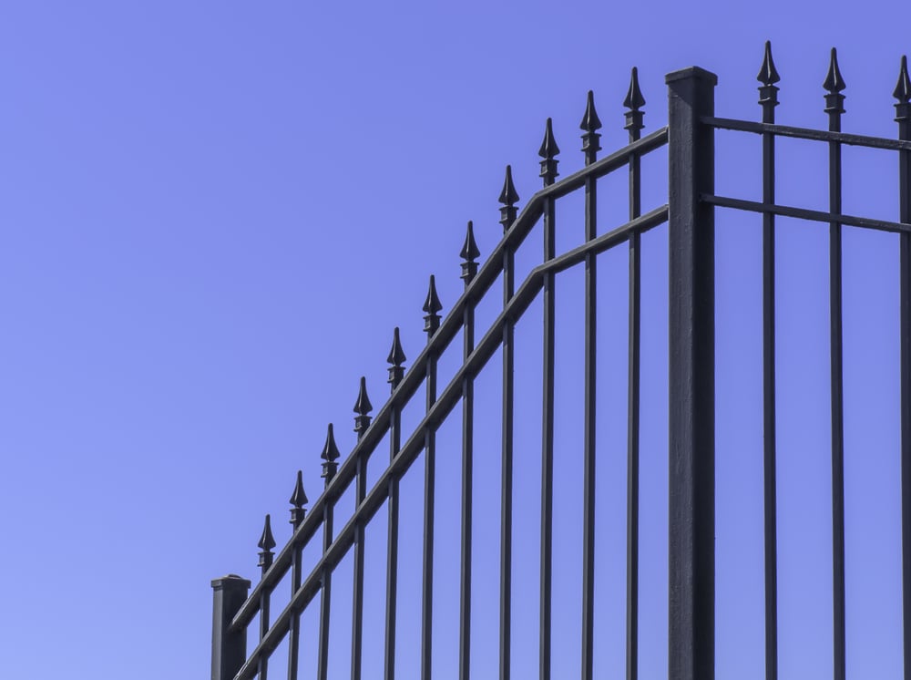 Section of wrought iron fence at top of hill with blue sky for copy space